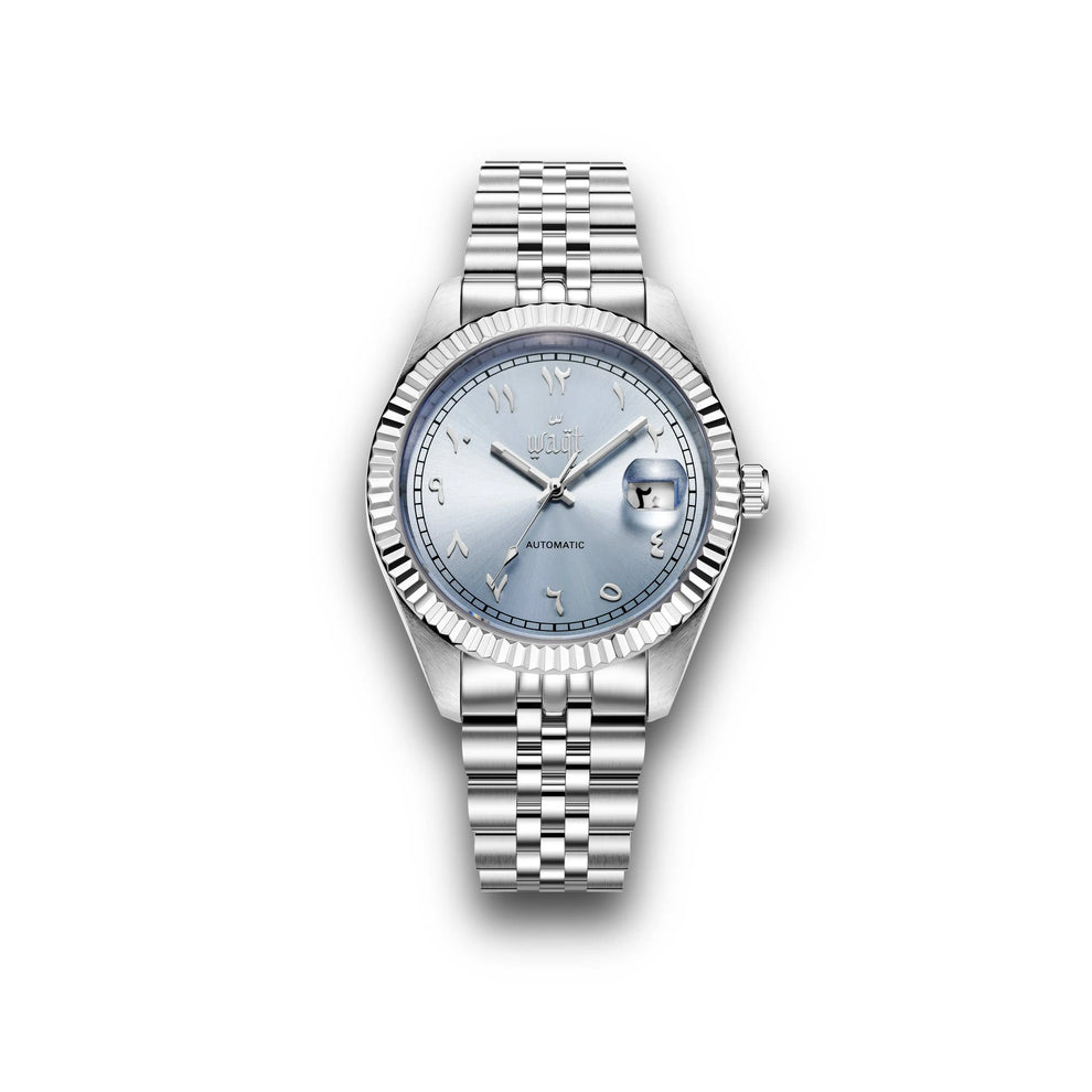 Vue de face rapprochée de la montre Waqt, dotée d'un cadran bleu ciel clair avec des chiffres arabes argentés, d'une lunette cannelée et d'un boîtier en acier inoxydable poli, qui capture le reflet doux de la lumière naturelle pour une finition raffinée et élégante.